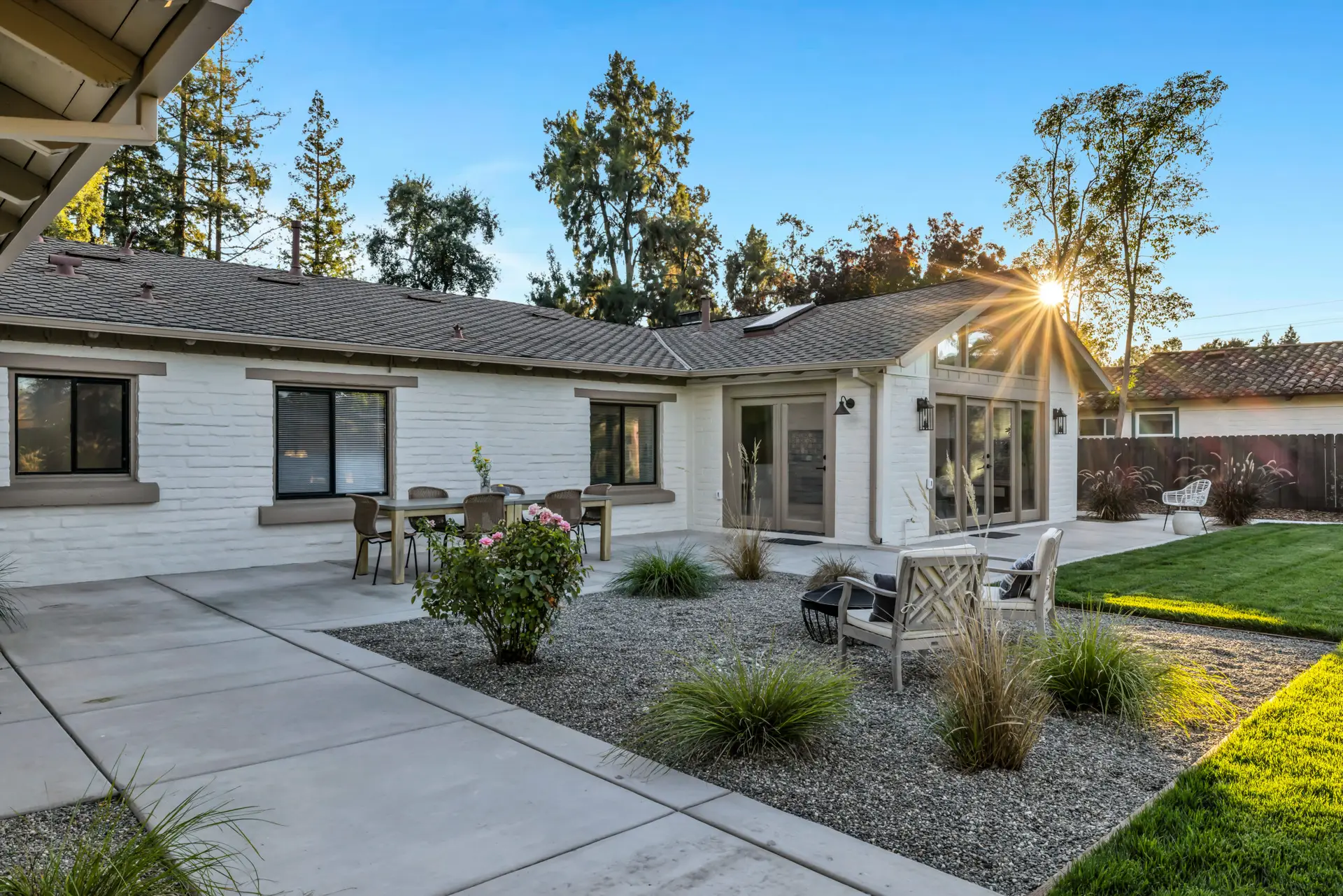 Exterior real estate photo of a modern Sacramento home with landscaped backyard, patio seating, and evening sun flare.